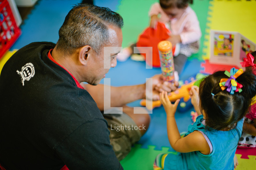 father playing with his toddler daughters in a playroom 