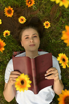 Portrait Of A Happy Girl With Flowers In Her Hair on Field holding a Bible 