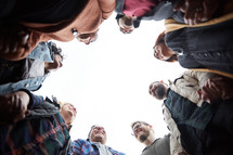 looking up into a group prayer circle with men and women holding hands in prayer in fall 