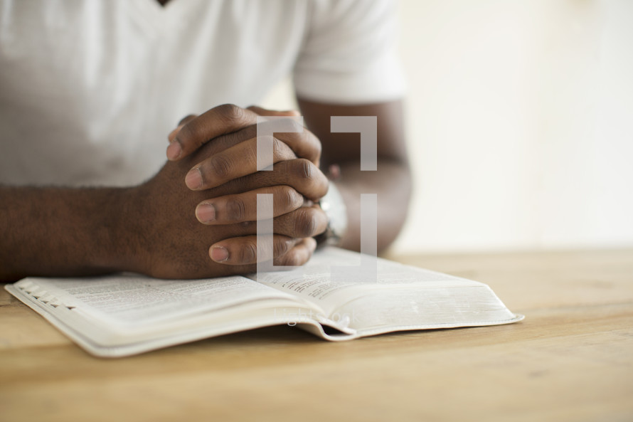 a man with praying hands over the pages of a Bible. 