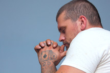 man with tattooed hands praying 