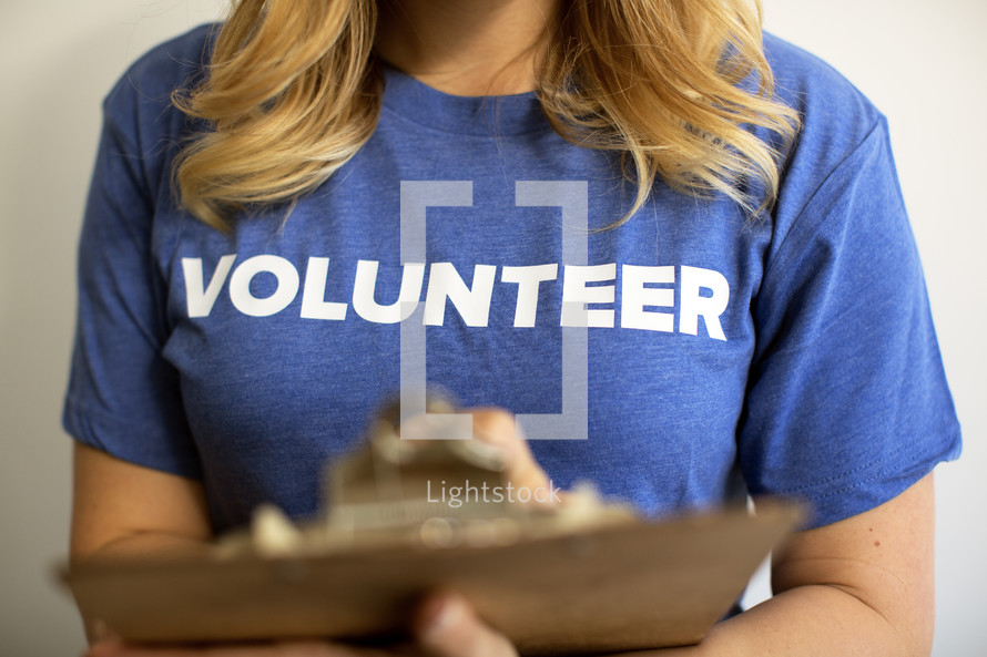 A woman with a clipboard wearing a blue t-shirt saying, "volunteer."