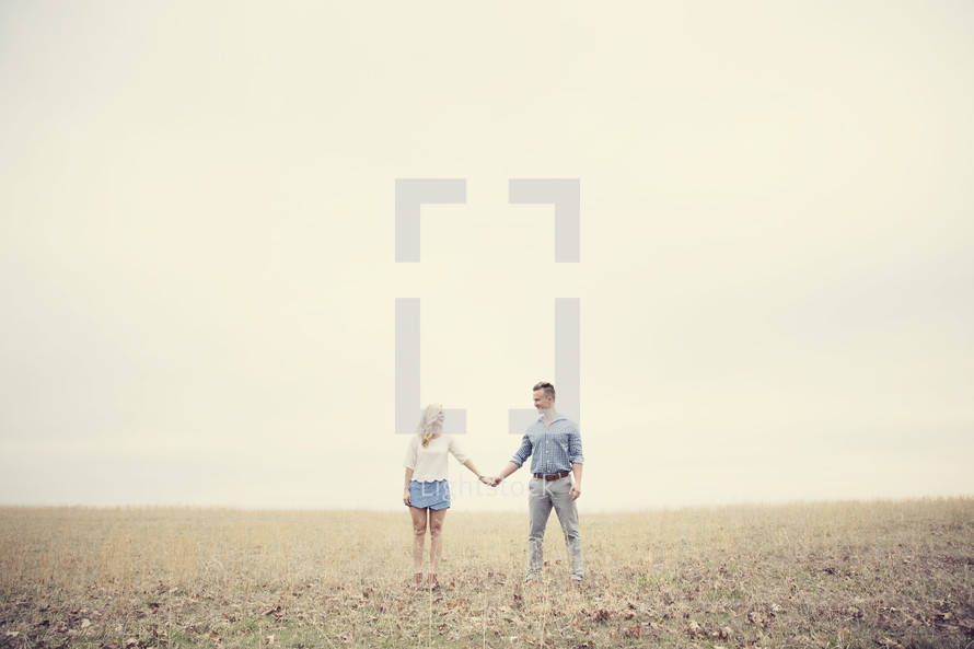 A man and woman holding hands in a field of grass.