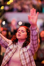 A young woman with arms raised in a worship service.