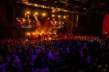 A large congregation in front of a stage lit by bright lights.