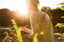 a woman journaling outdoors at sunset 