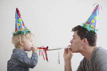 A man and toddler boy wearing party hats.  
