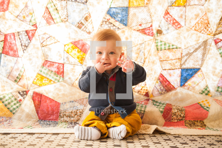 infant boy sitting and sucking on his fingers 