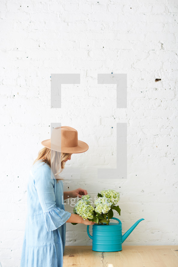 a woman arranging hydrangeas in a watering can on a table 