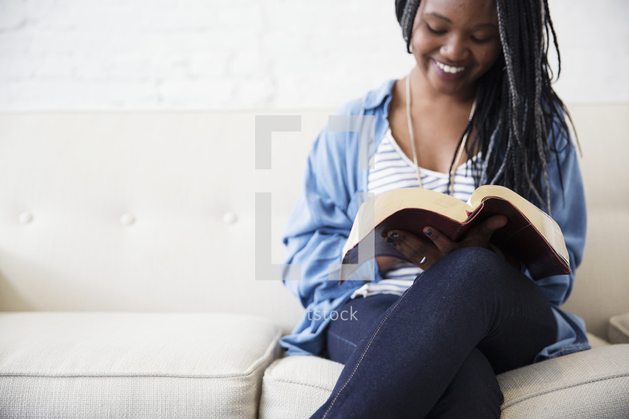 a young woman sitting on a couch reading a Bible 