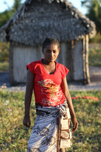 young woman standing in front of a hut 