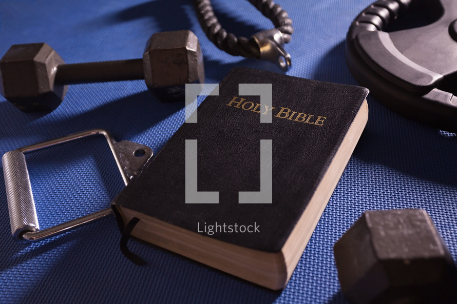 Holy Bible surrounded by dumbbells weights and other exercise equipment