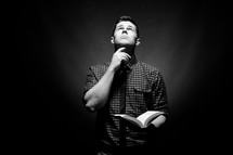man holding a Bible with his hand under his chin looking up to God