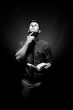 man holding a Bible with his finger under his chin and looking up to God