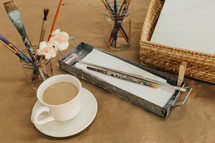 coffee with creamer and paint brushes in mason jars on a table in an art studio 
