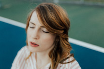 a woman with eyes closed in prayer sitting on a tennis court 