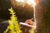 a woman journaling outdoors at sunrise.
