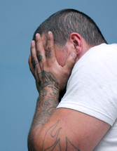 man with tattooed hands covering his face