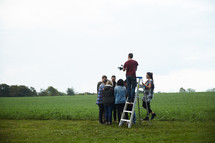 man on a ladder photographer a group praying in a circle 