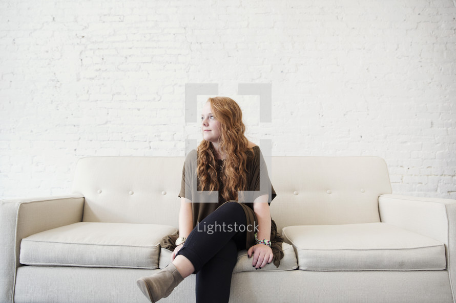 a young woman sitting on a couch thinking 