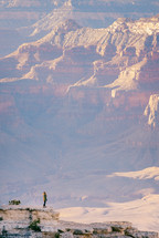a woman standing at the edge of a cliff looking out at canyons 