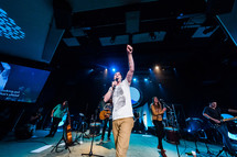 Worship leader raising fist in praise on stage, tattooed arm, youth, generation 