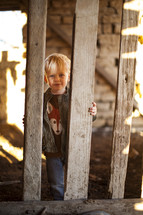 A toddler boy looking through the pickets of a fence. 
