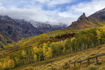 clouds over mountain peaks and fall trees on a mountainside 