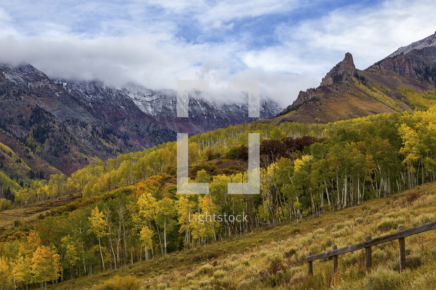 clouds over mountain peaks and fall trees on a mountainside 