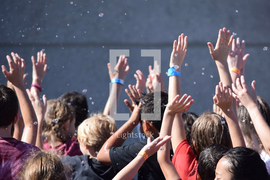 kids with hands raised getting wet from splashing water at summer camp