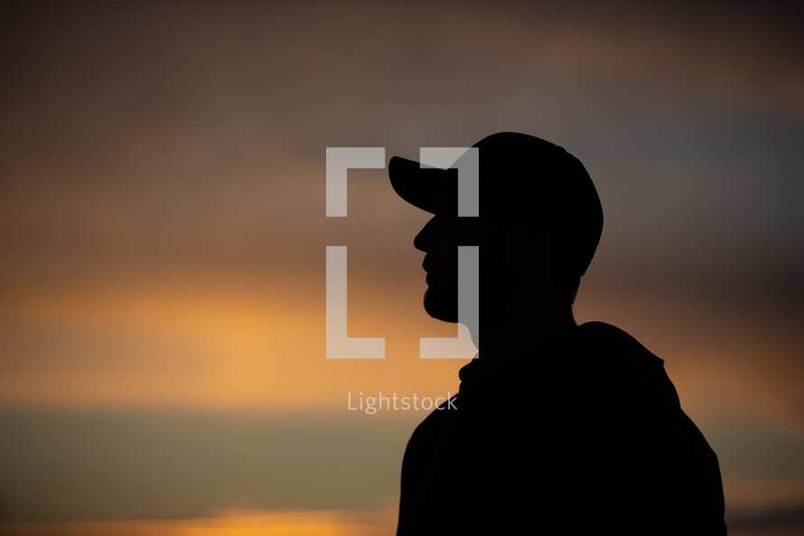silhouette of a man in a ball cap at sunset 