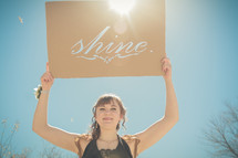 woman holding up a sign in sunlight with the words shine