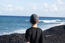 boy standing on a volcanic beach 