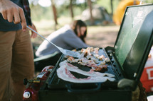 a man flipping bacon on a camping grill 