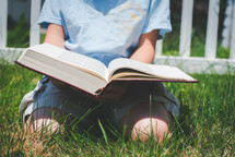 a boy kneeling in the grass reading a Bible 