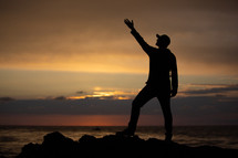 silhouette of a man with hand raised standing on a shore 