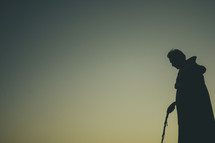 silhouette of a man in a robe and a walking stick 
