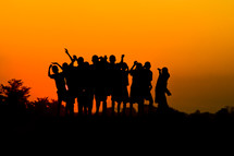 silhouettes of children with raised hands at sunset 
