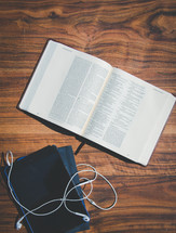 open Bible, tablet, and earbuds on a wood table 