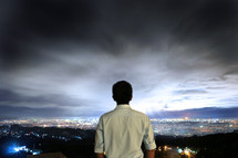 man with his back to the camera looking out over a city at night 