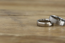 Two men's wedding rings on a wooden table.
