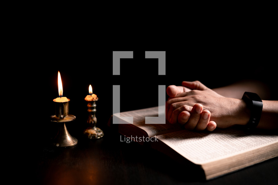 Bible and candlelight with praying hands