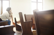 a woman sitting in a church pew praying 