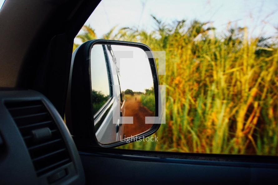 view in a rearview mirror of a dirt road 