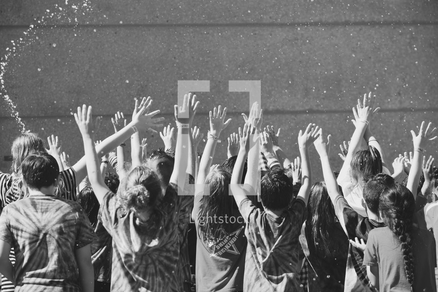 children with hands raised being splashed by water 