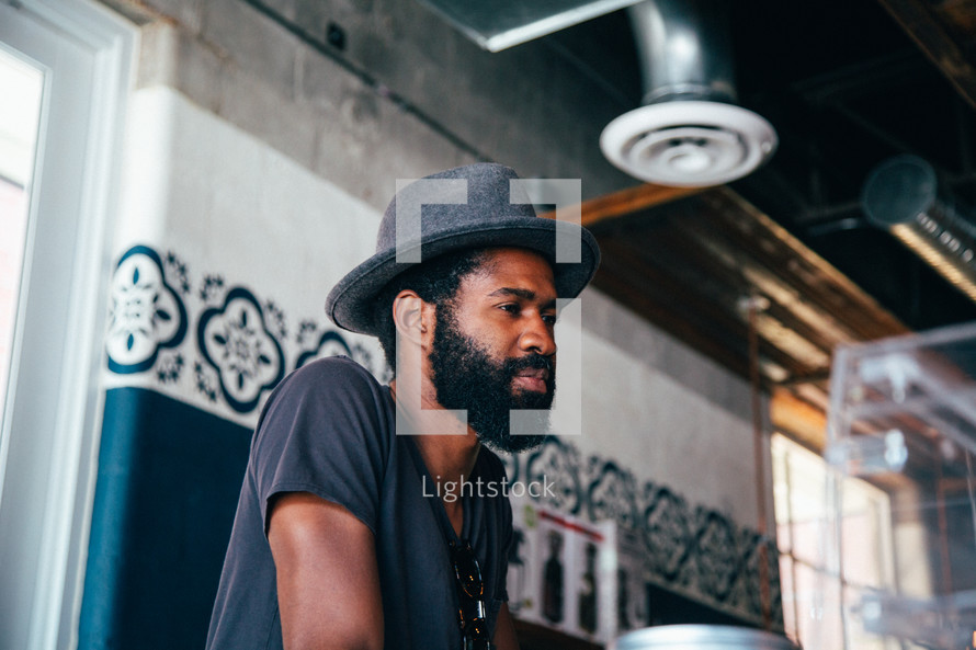 side profile of a man in a hat and beard sitting in a coffee shop