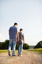a father and son walking down a dirt road talking 