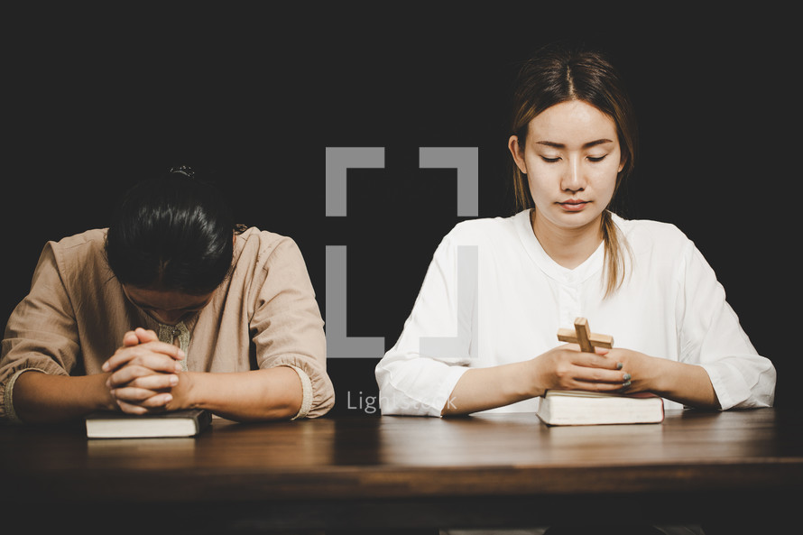 Two Asian women praying together with a cross and Bibles