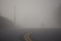 man riding a bicycle across a street under thick fog