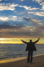 man with raised hands on a beach 